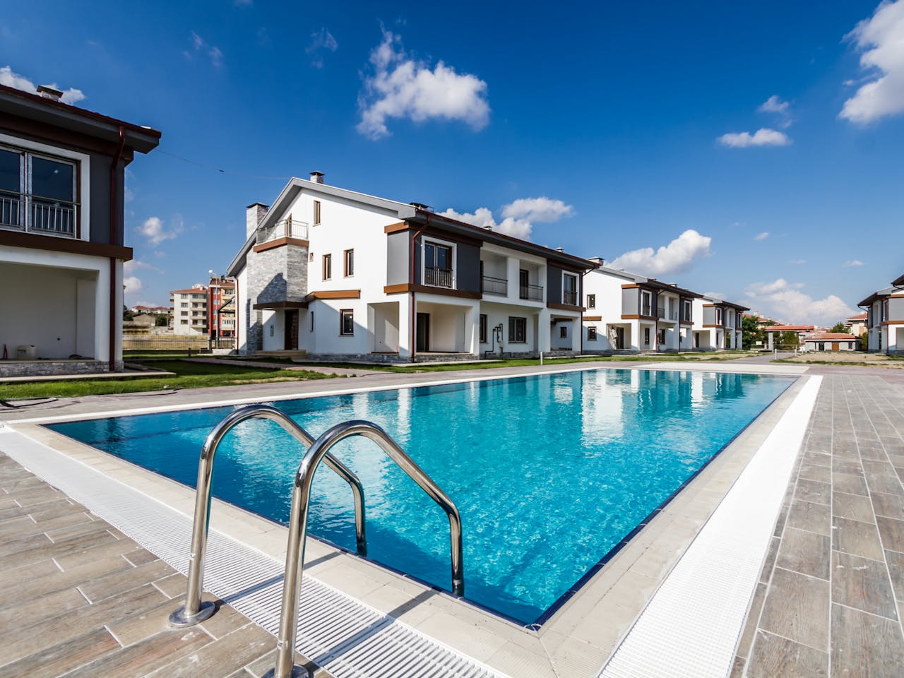 about-01 Luxury modern villas surrounding a glistening swimming pool under a clear blue sky.