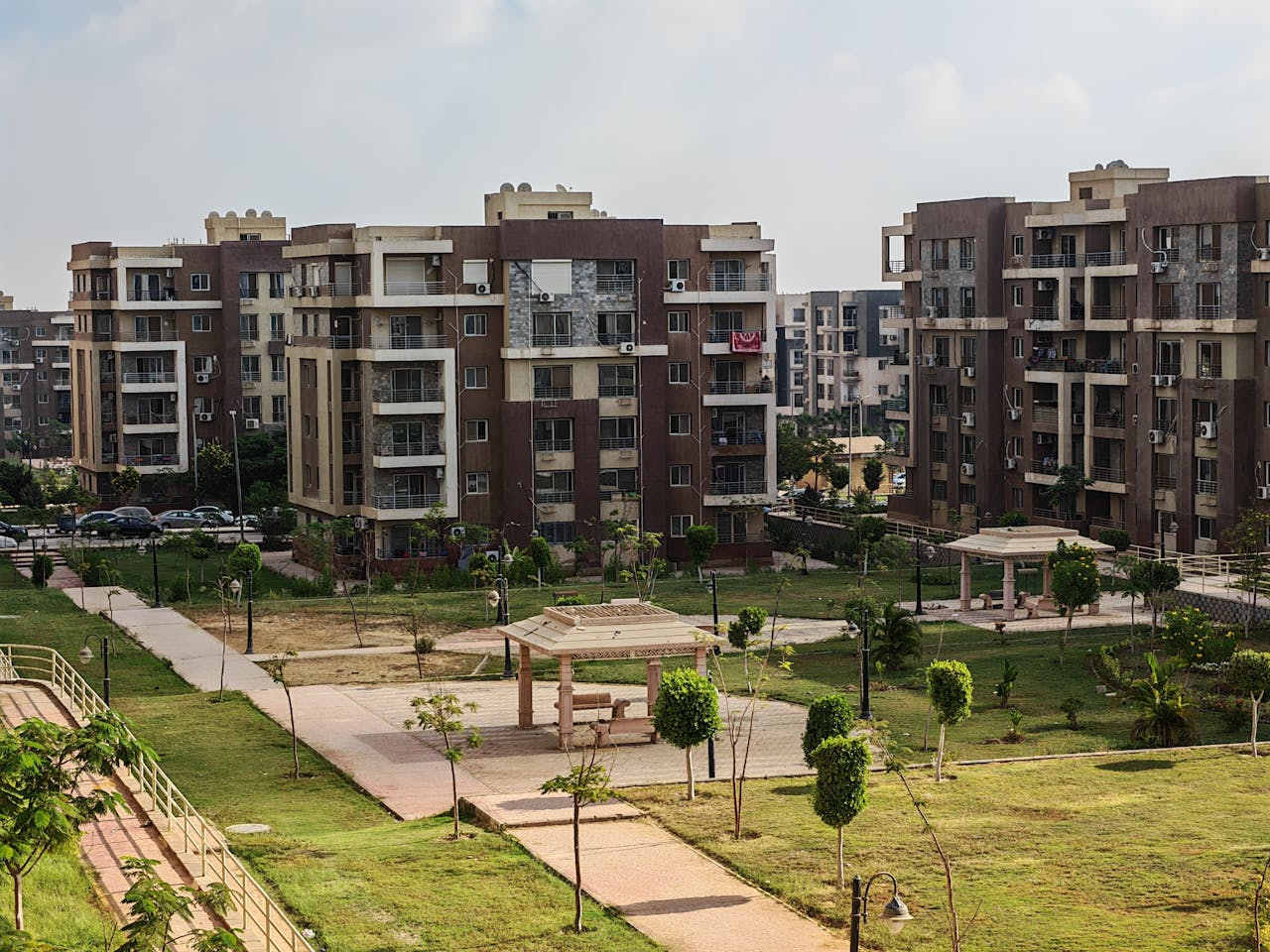 hero-img-01 A modern apartment complex featuring green urban park with pathways and recreational structures.
