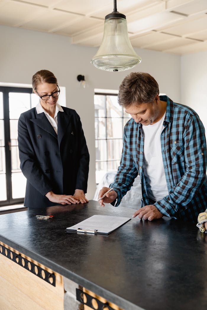 gallery-5 A businesswoman guides a homeowner through property signing at a kitchen counter.